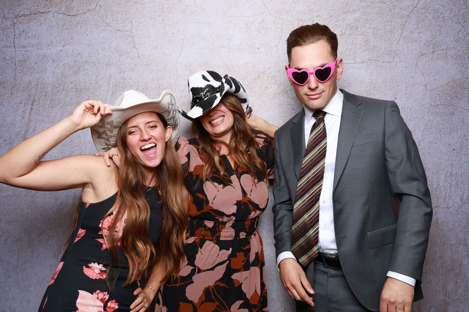 Three people pose with props and sunglasses in a festive photo booth setting.