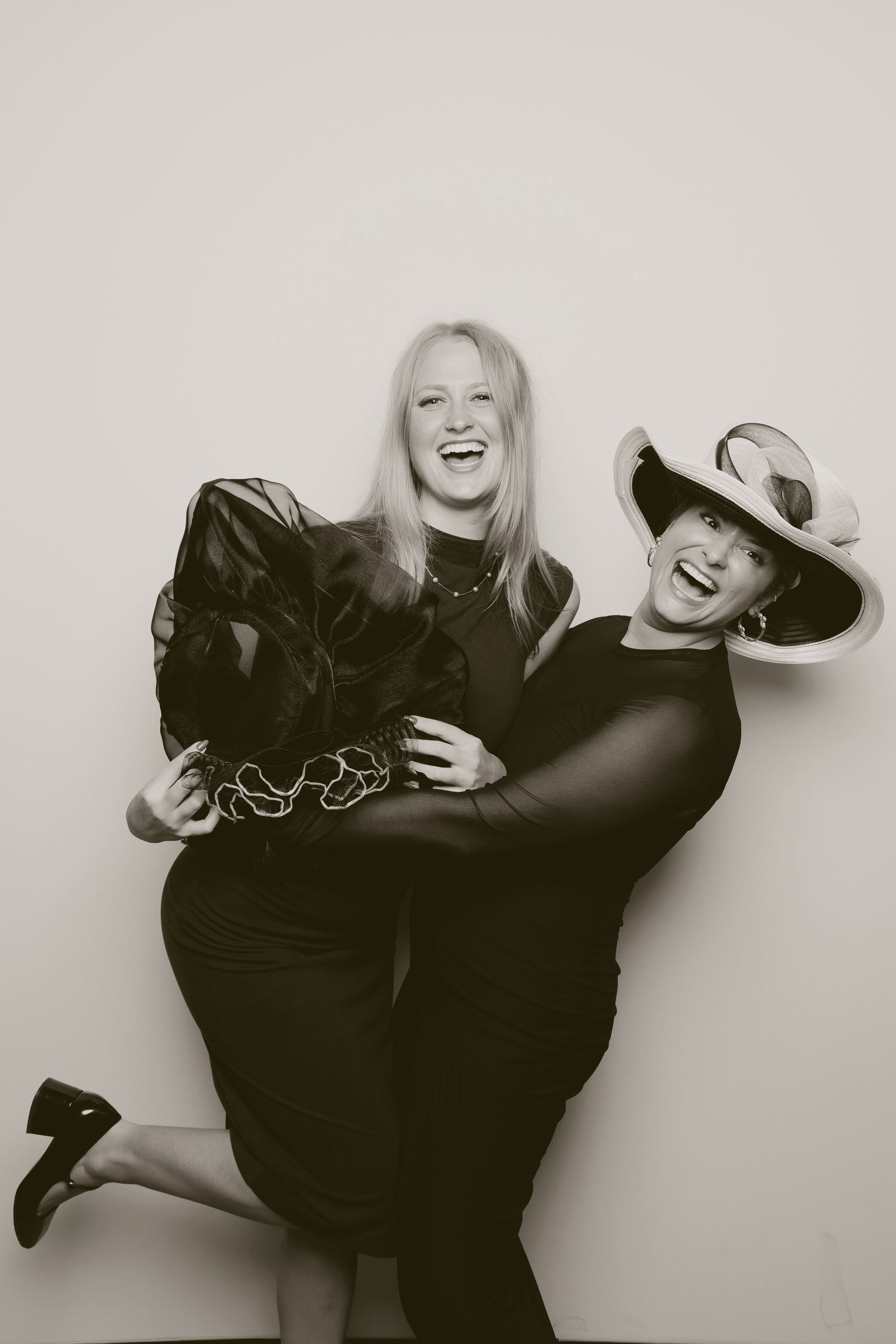 Two friends in black outfits strike playful pose during photo booth session.
