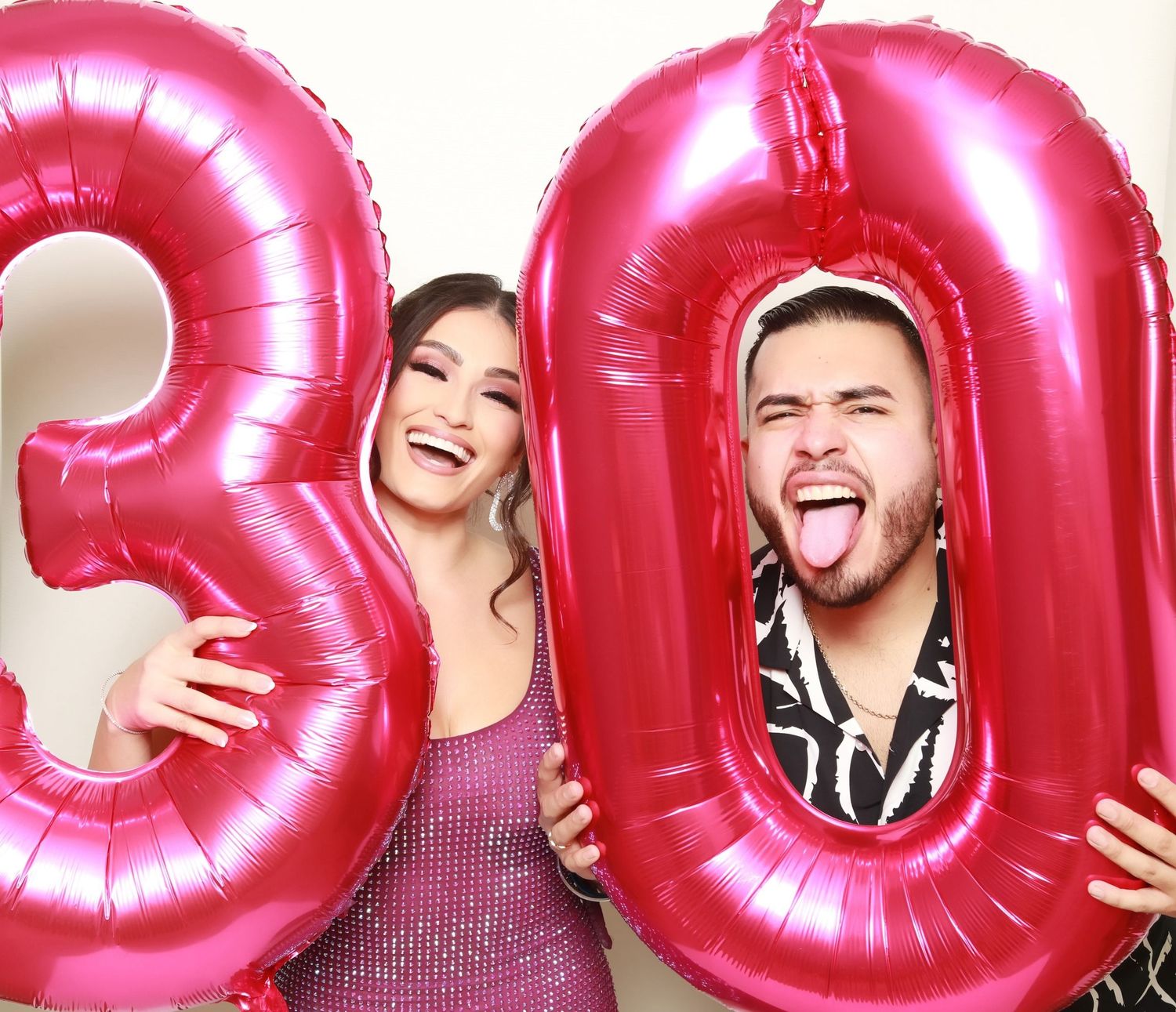 Two people pose with large pink metallic number 30 balloons for a birthday celebration.