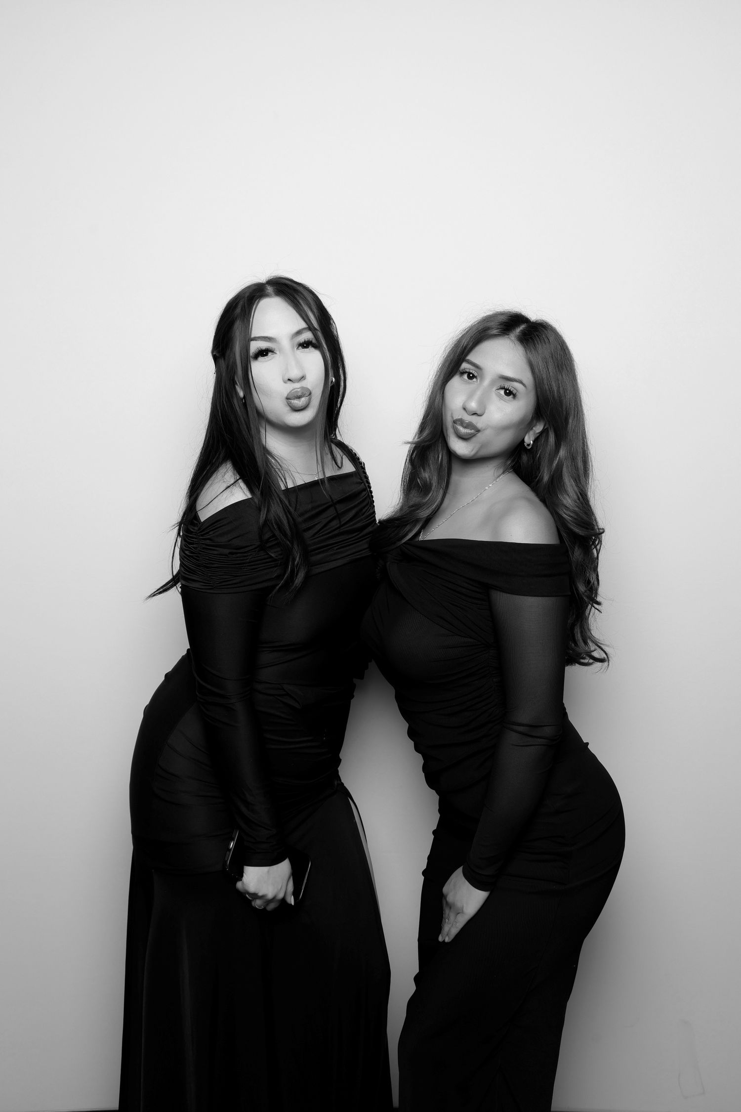 Two women in black dresses make playful expressions in photo booth.
