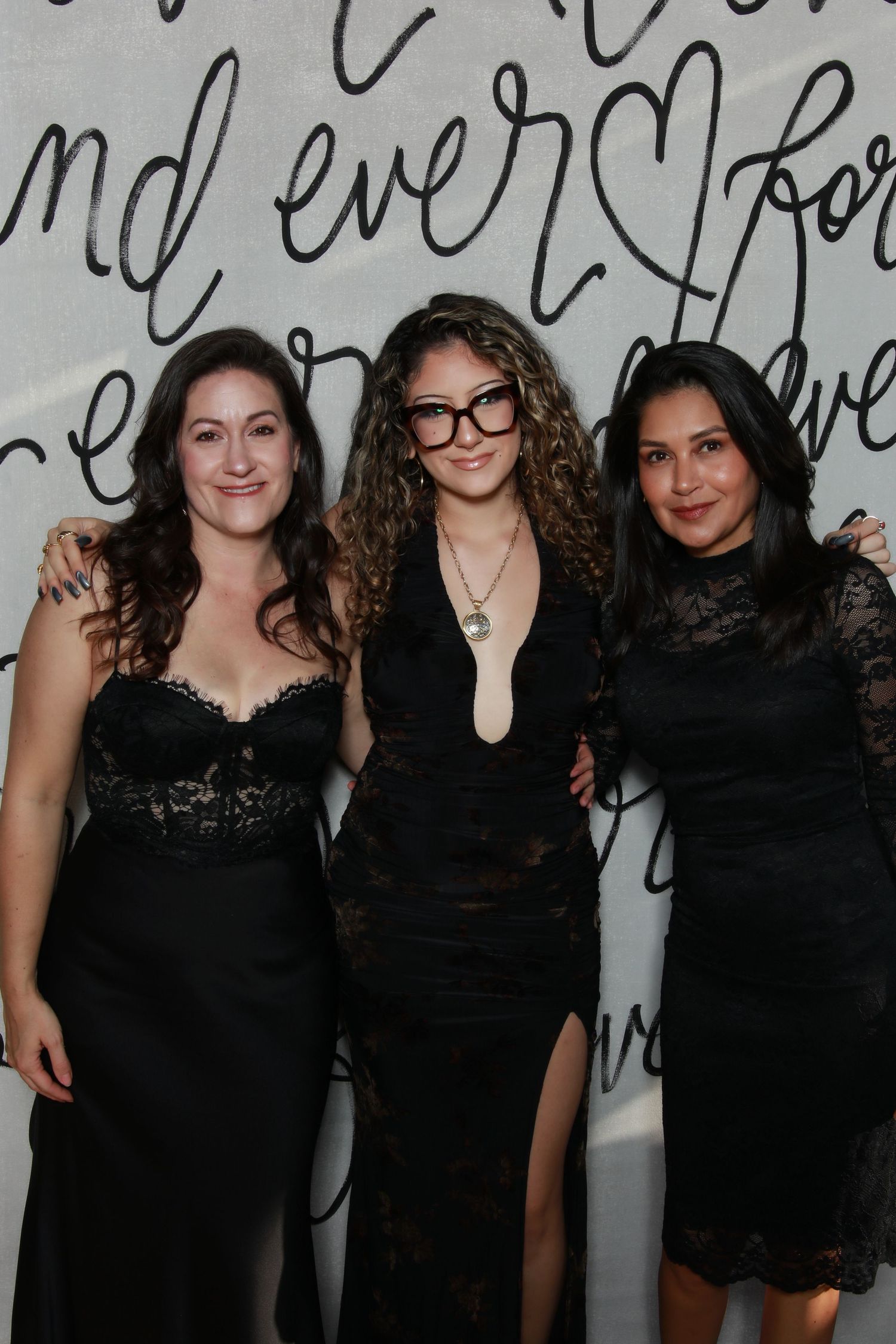 Group of friends in black dresses pose together against a wall with script writing.
