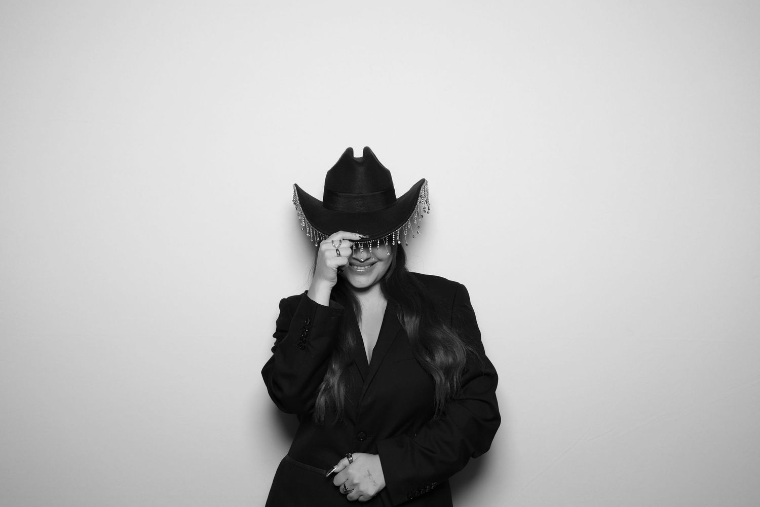 A person in a black suit and cowboy hat poses in a black and white photo booth shot.