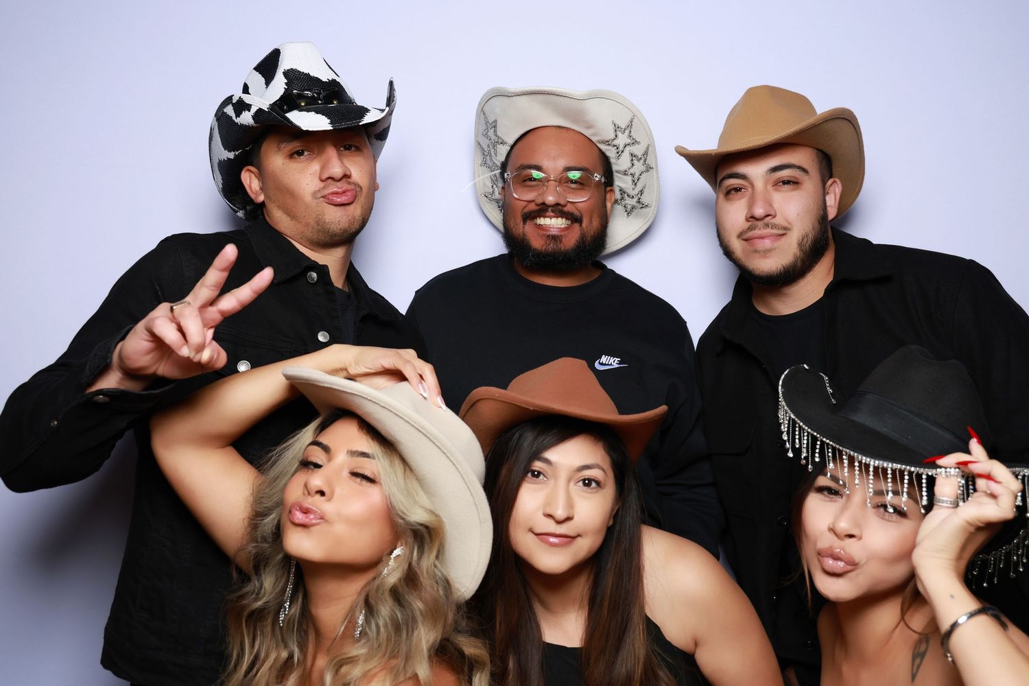 Six friends pose playfully in cowboy hats and casual attire at a photo booth.