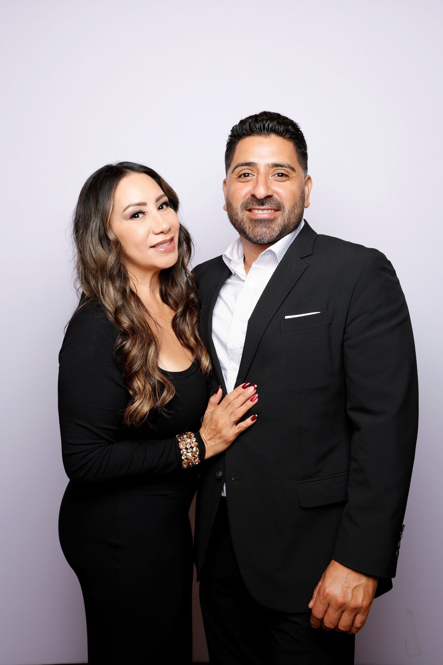 Couple in formal black attire poses elegantly against studio backdrop.