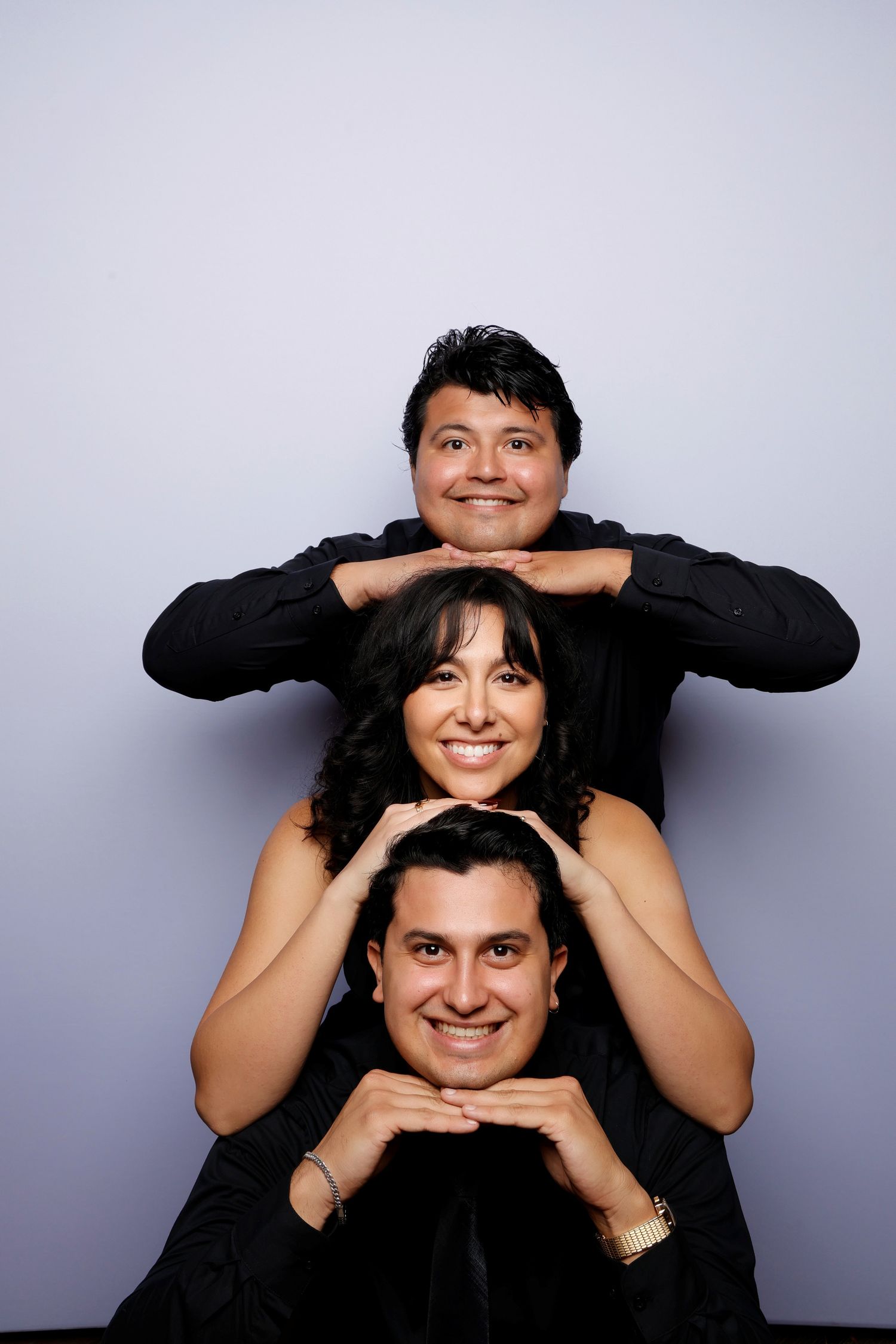 Three people posing playfully with stacked heads and hands in a studio photo booth setting.