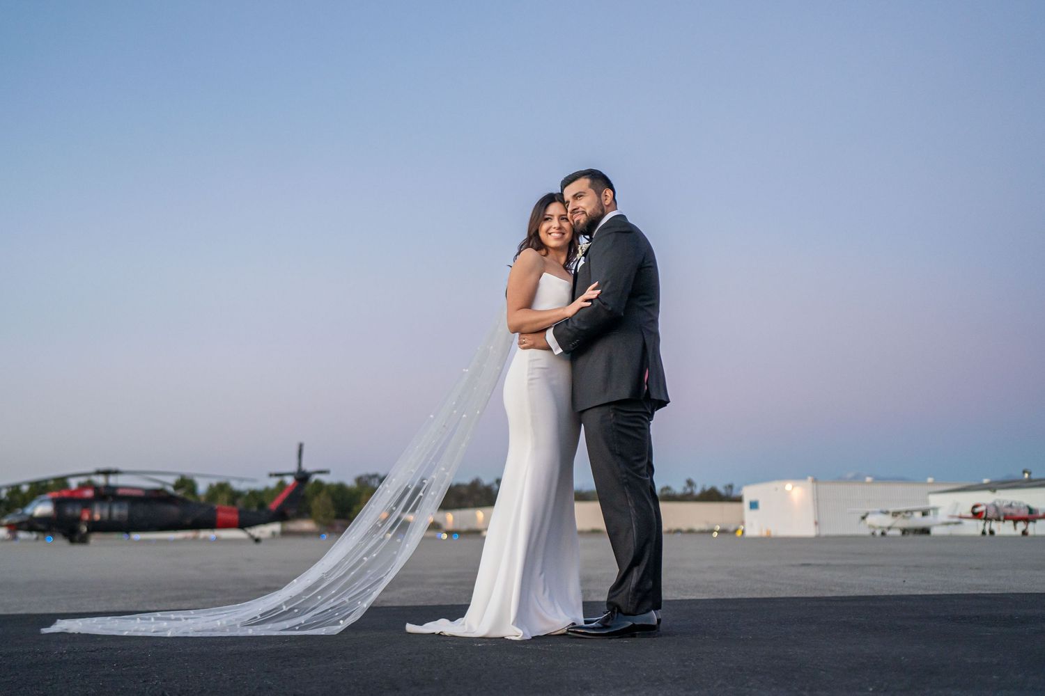 Wedding couple embracing at sunset with airfield in background.