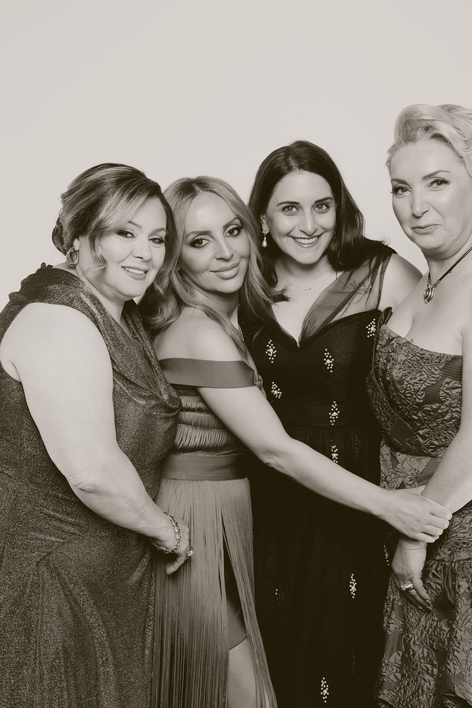 Four elegantly dressed women posing together in black and white photo at formal event.