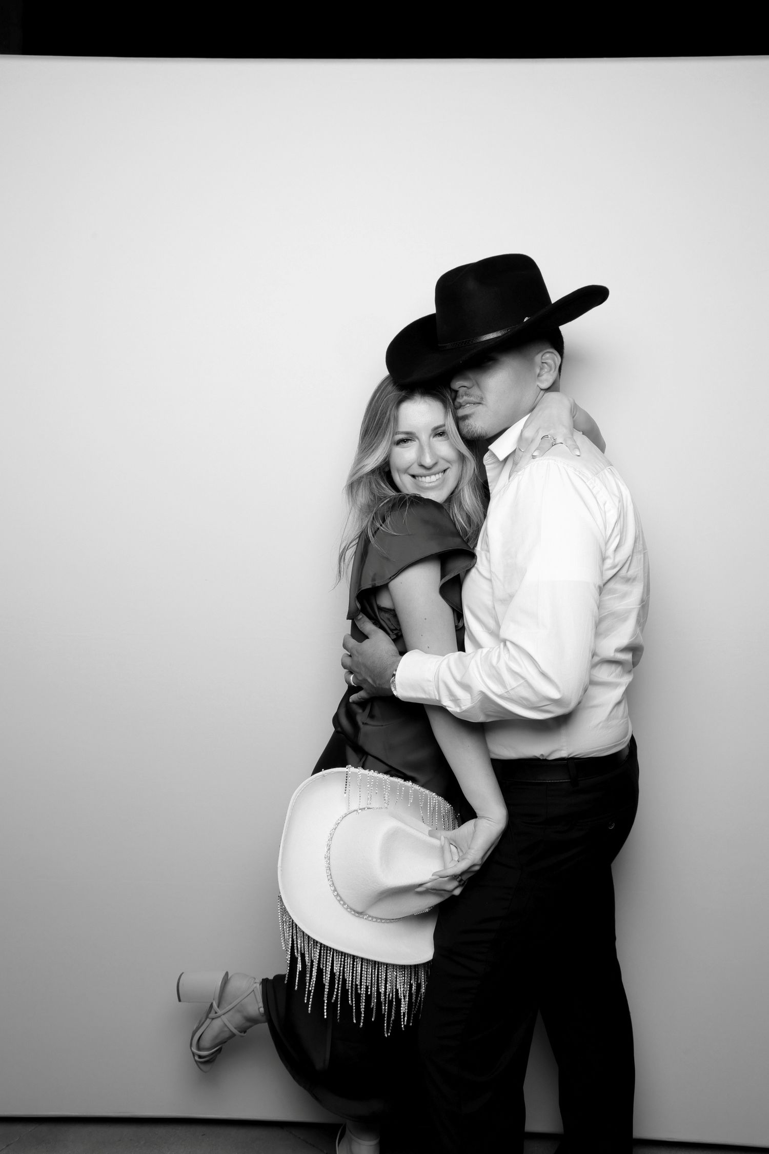 A western-styled couple embraces in a black and white photo booth portrait.
