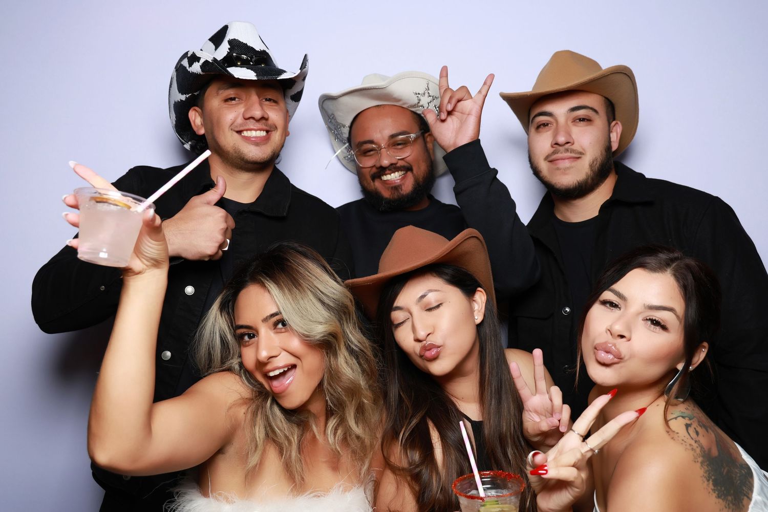 A group of friends in cowboy hats and party attire pose together in a photo booth.