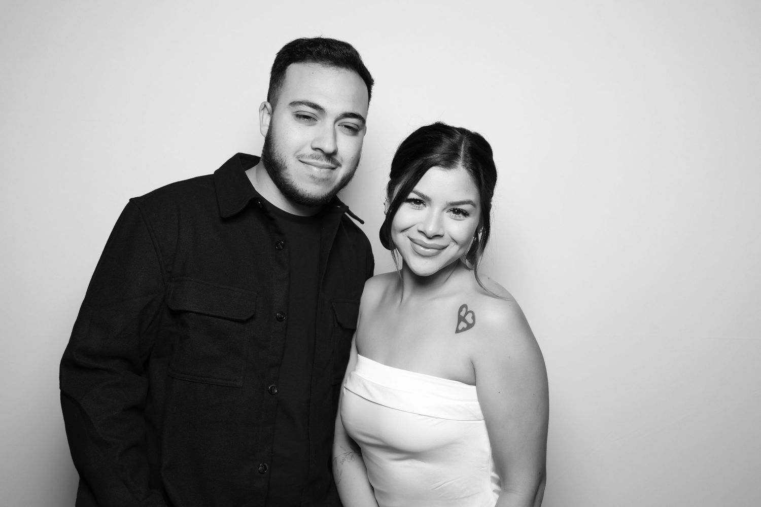 A couple poses together in formal attire for a black and white photo booth portrait.