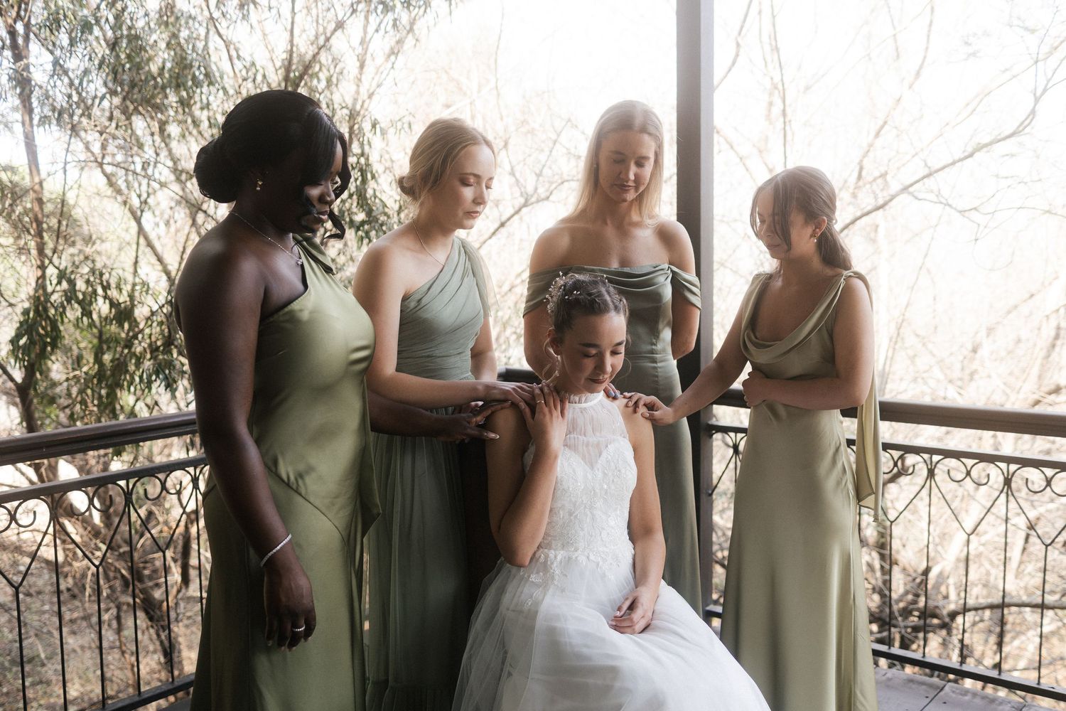 Bride with bridesmaids in sage green dresses on balcony praying with bride in Western Cape wedding