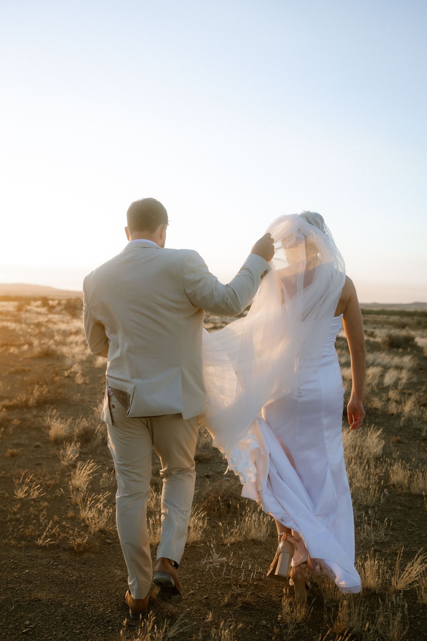 Bride and groom walking in sunlit field at sunset, South Africa wedding videographer