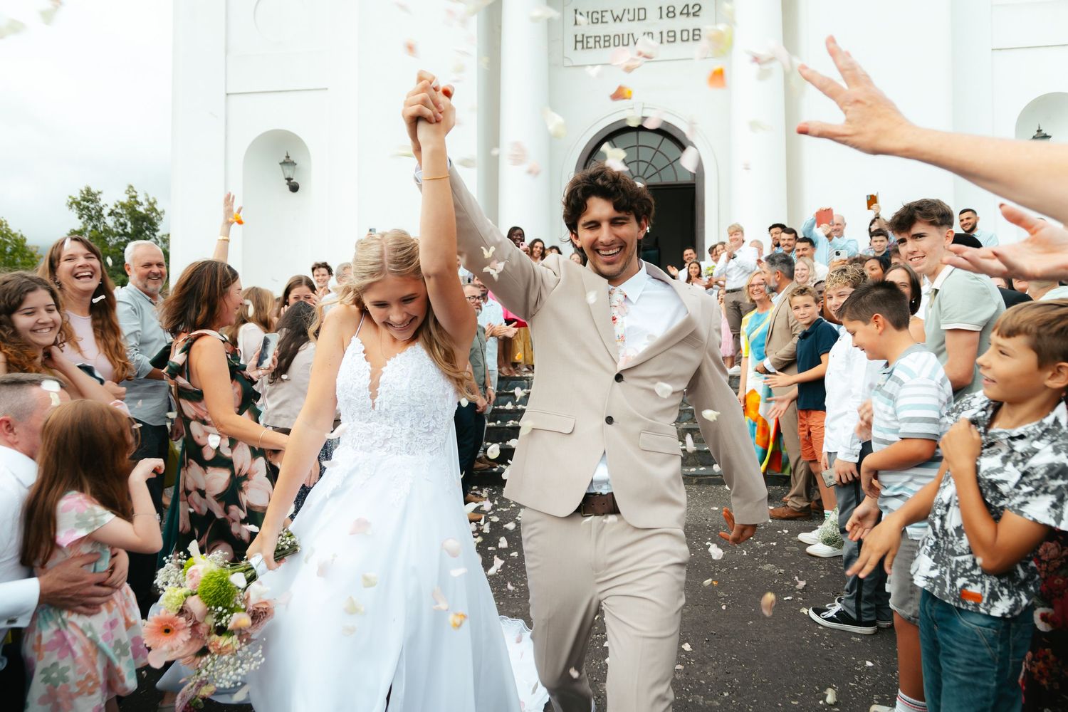 Newlywed couple walking out of church with guests throwing petals, Garden Route wedding photo and film
