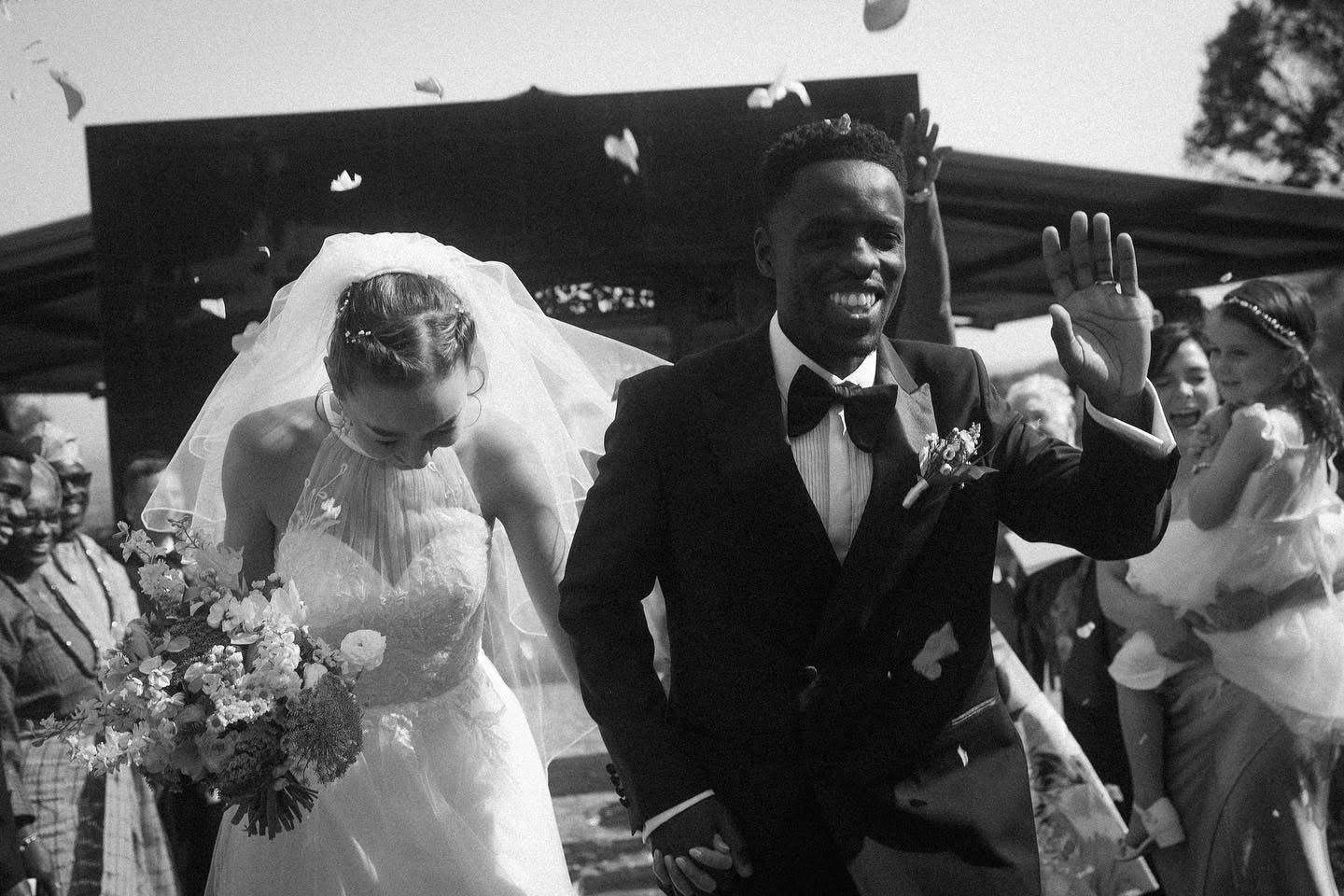 Newlywed couple walking outdoors with guests throwing flower petals, South Africa wedding photo and film