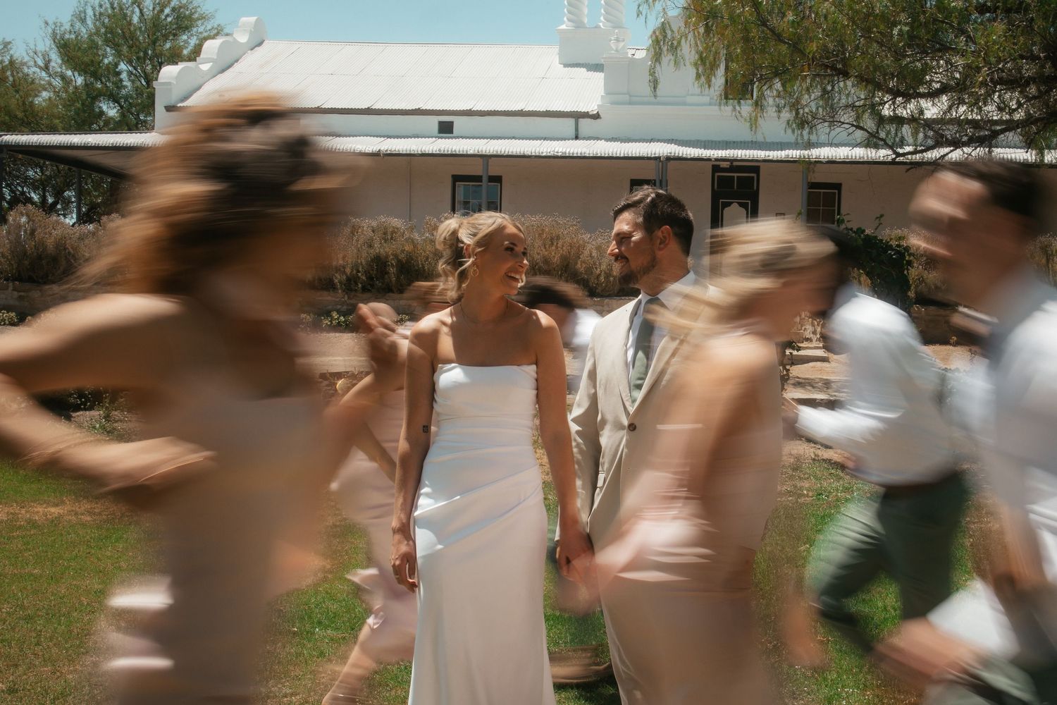 Bride and groom holding hands outdoors with blurred wedding guests in Western Cape engagement photography