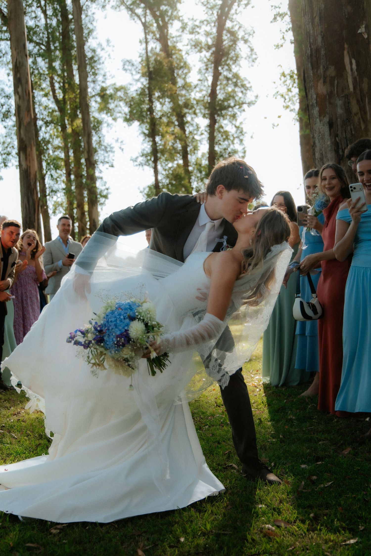 Bride and groom kissing outdoors at wedding with guests and trees, Garden Route wedding photographer