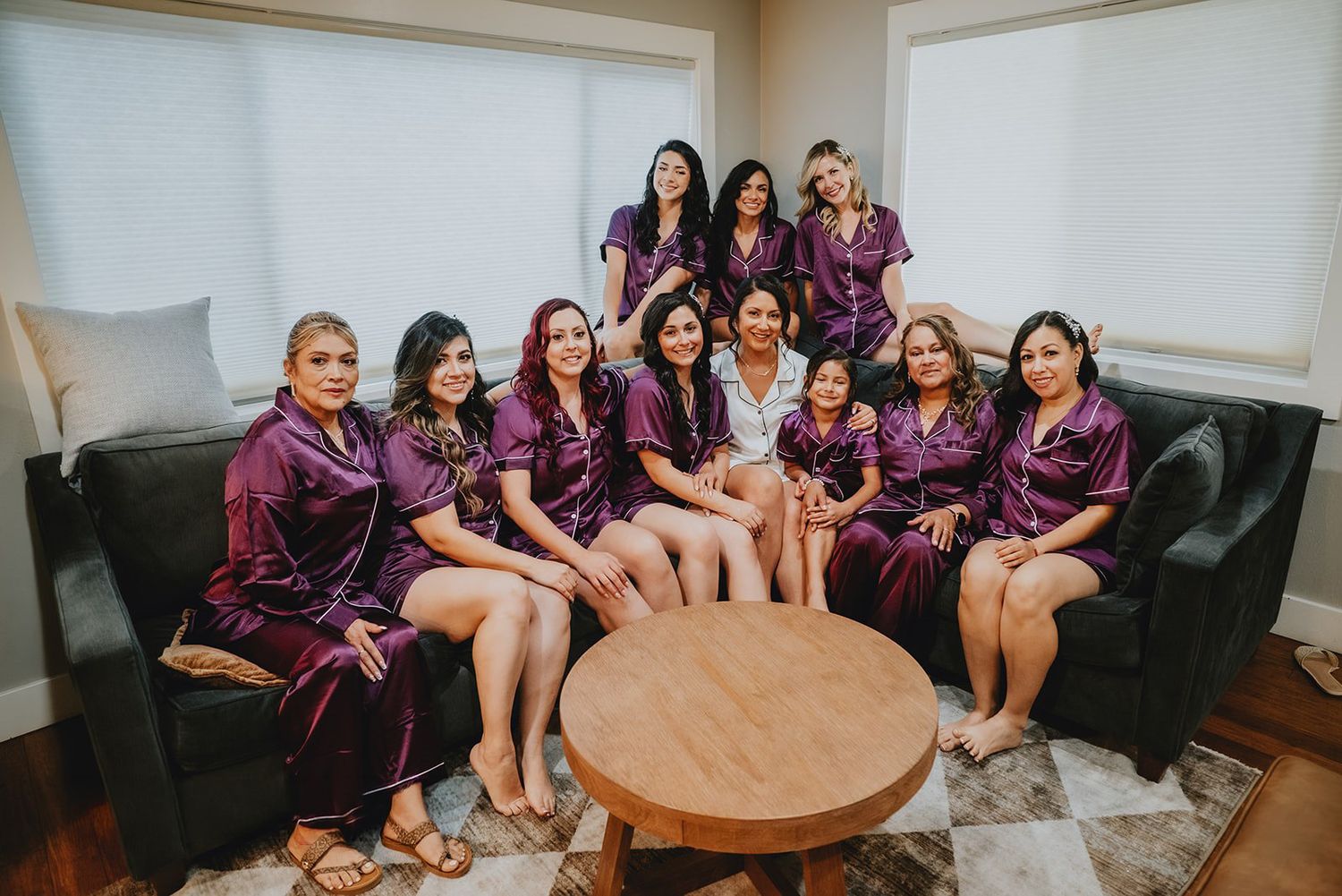 Group of bridesmaids in matching purple satin robes posing together on a couch during wedding preparations.