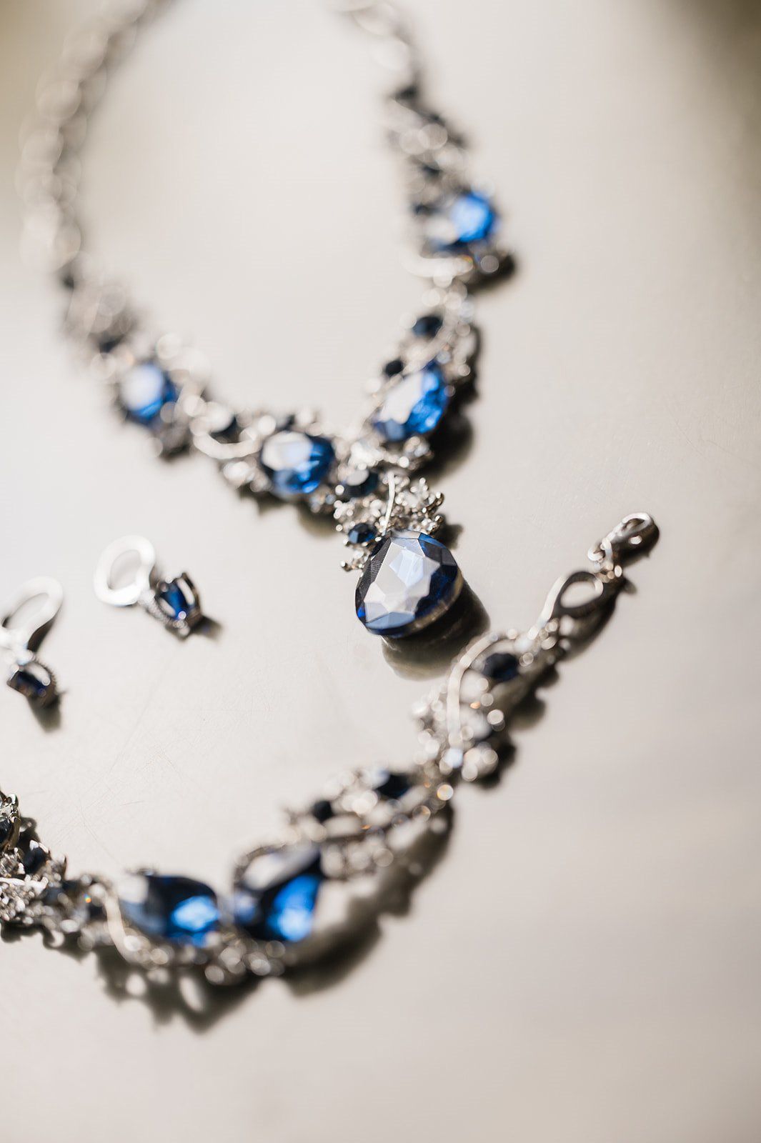 Elegant silver necklace, bracelet, and earrings set featuring sparkling blue gemstones on a light background.