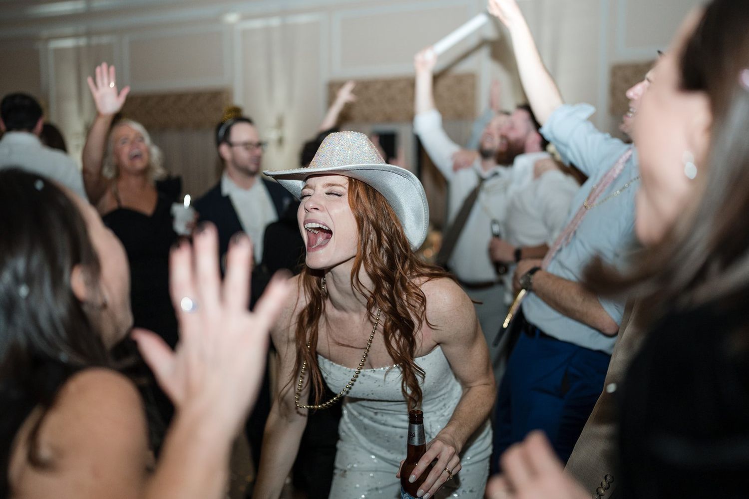 Joyful woman in white cowboy hat dancing and singing at a lively wedding reception party.