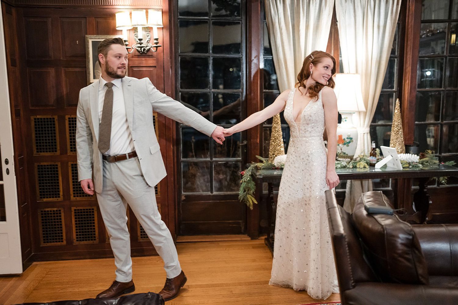 Bride and groom hold hands during first dance in elegant wood-paneled indoor wedding venue.