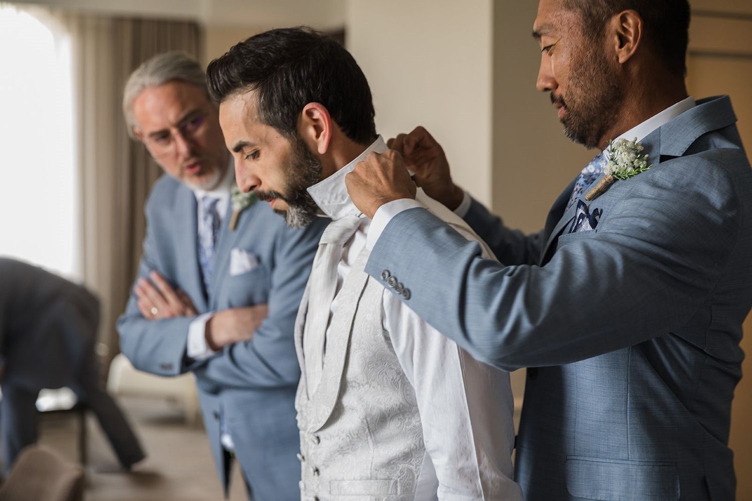 Groomsmen helping groom put on his vest before the wedding ceremony.