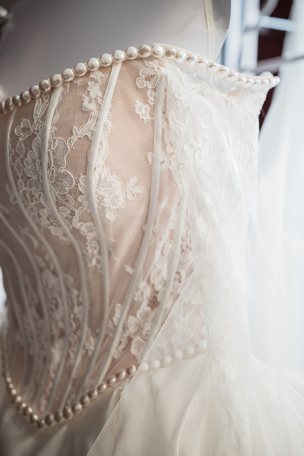 Close-up of an elegant wedding dress on a mannequin featuring intricate lace corset bodice adorned with pearl buttons.