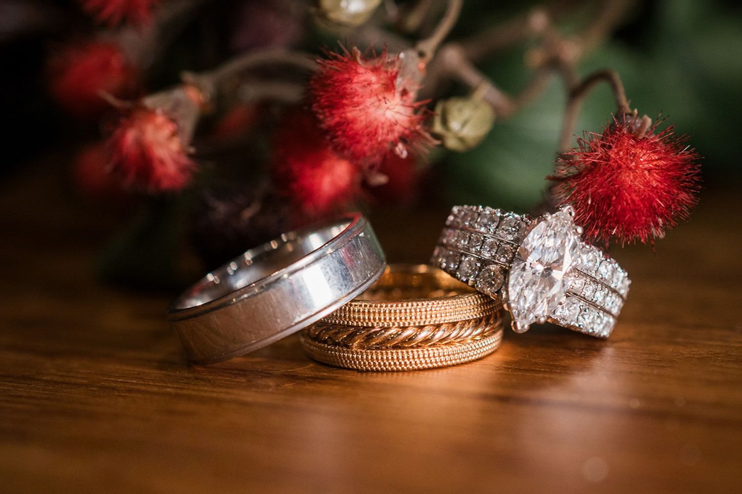 Three wedding rings and a diamond engagement ring set on a wooden table with red flowers in the background.