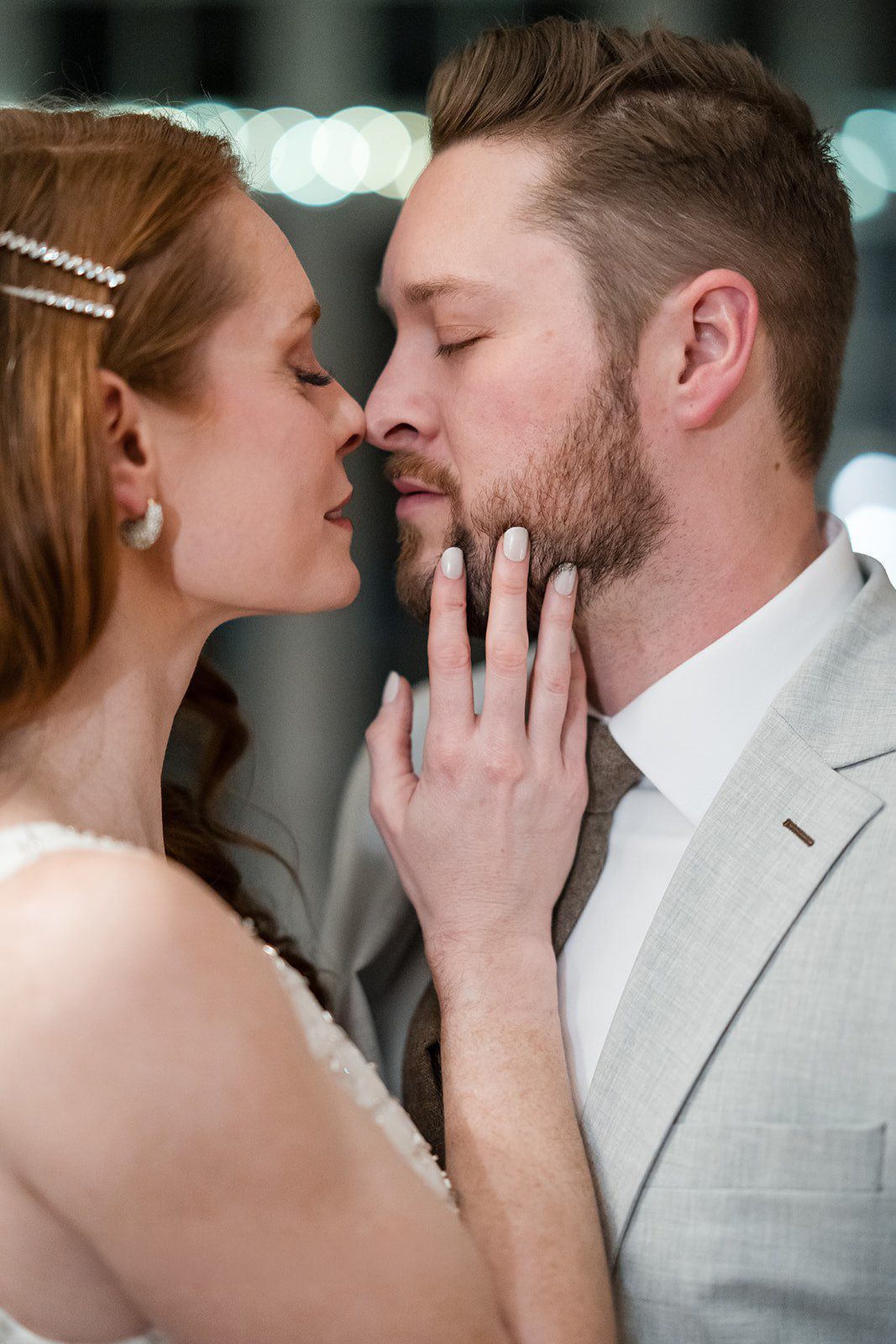 A bride and groom share a romantic kiss, with the bride gently holding the groom's bearded face during their wedding.