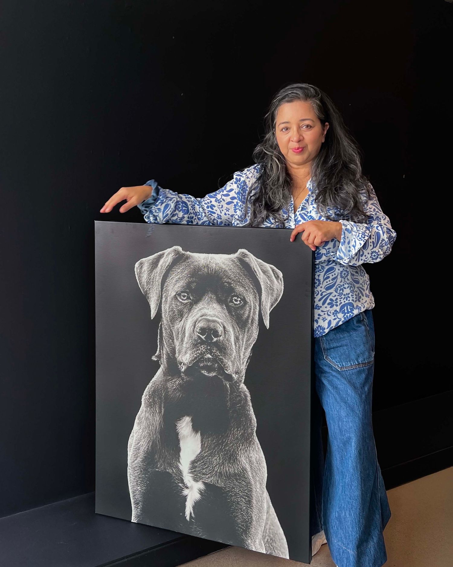 Boutique pet photography wall art canvas featuring black dog portrait, that Anu Kalle is holding  up to show scale of artwork.