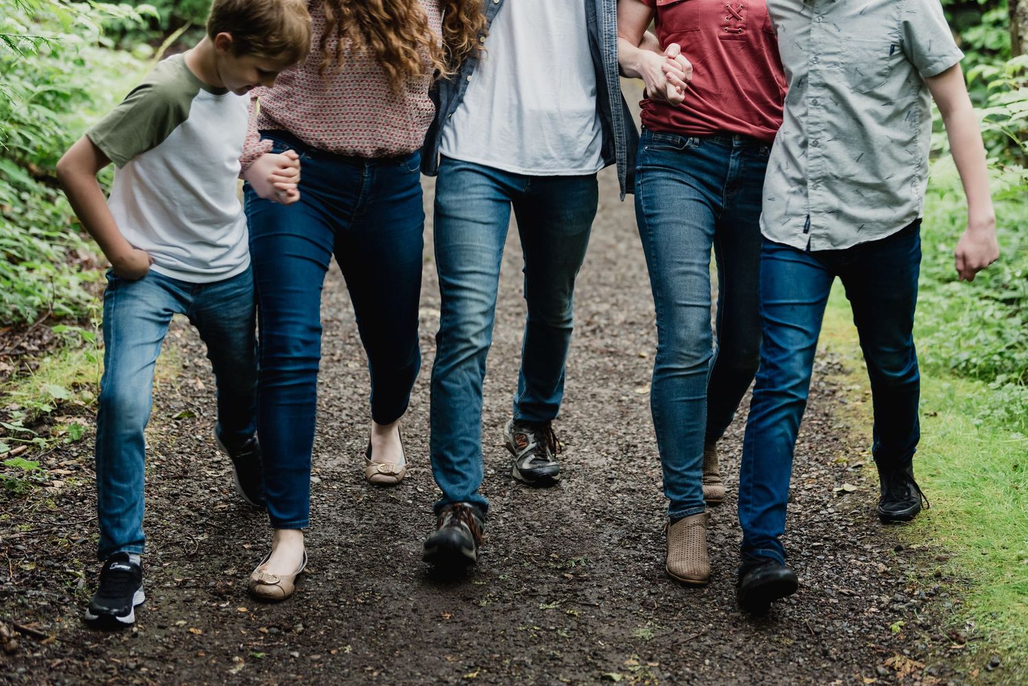 Group of people walking together on a forest path wearing casual clothing and jeans.