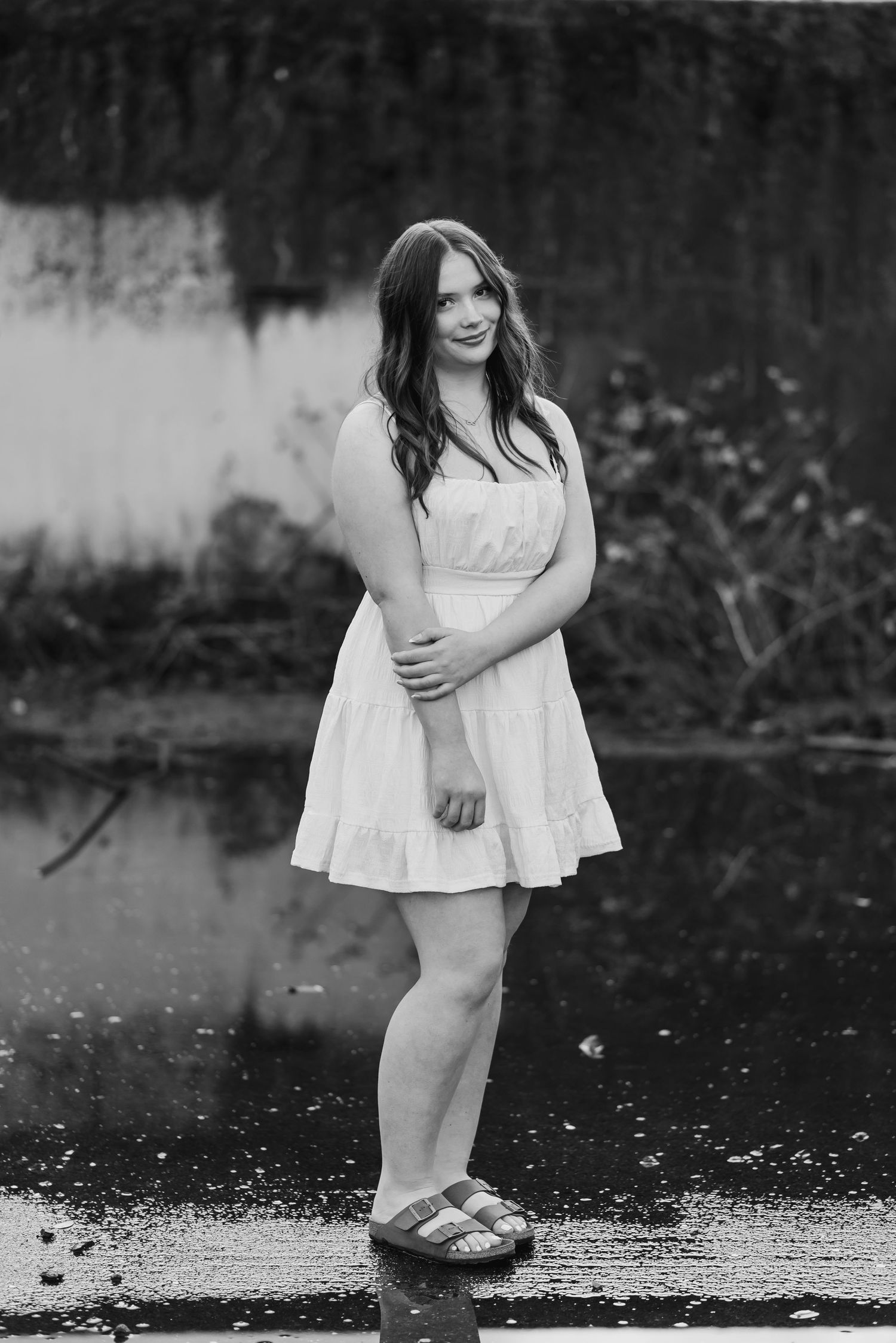 A series of black and white photographs showing a person in a white dress standing near water in moody lighting.