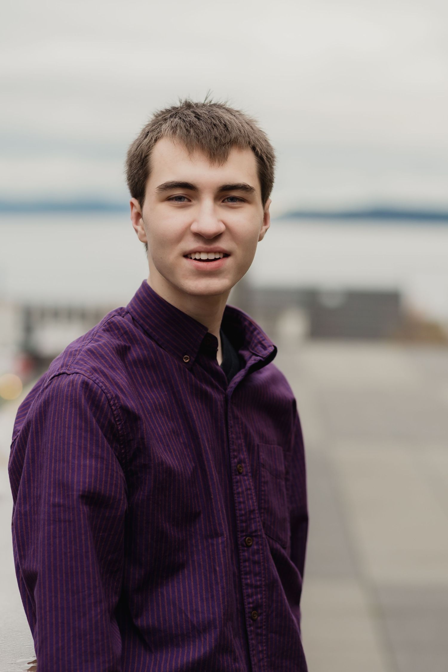 A person in a purple corduroy jacket stands outdoors against a blurred background.