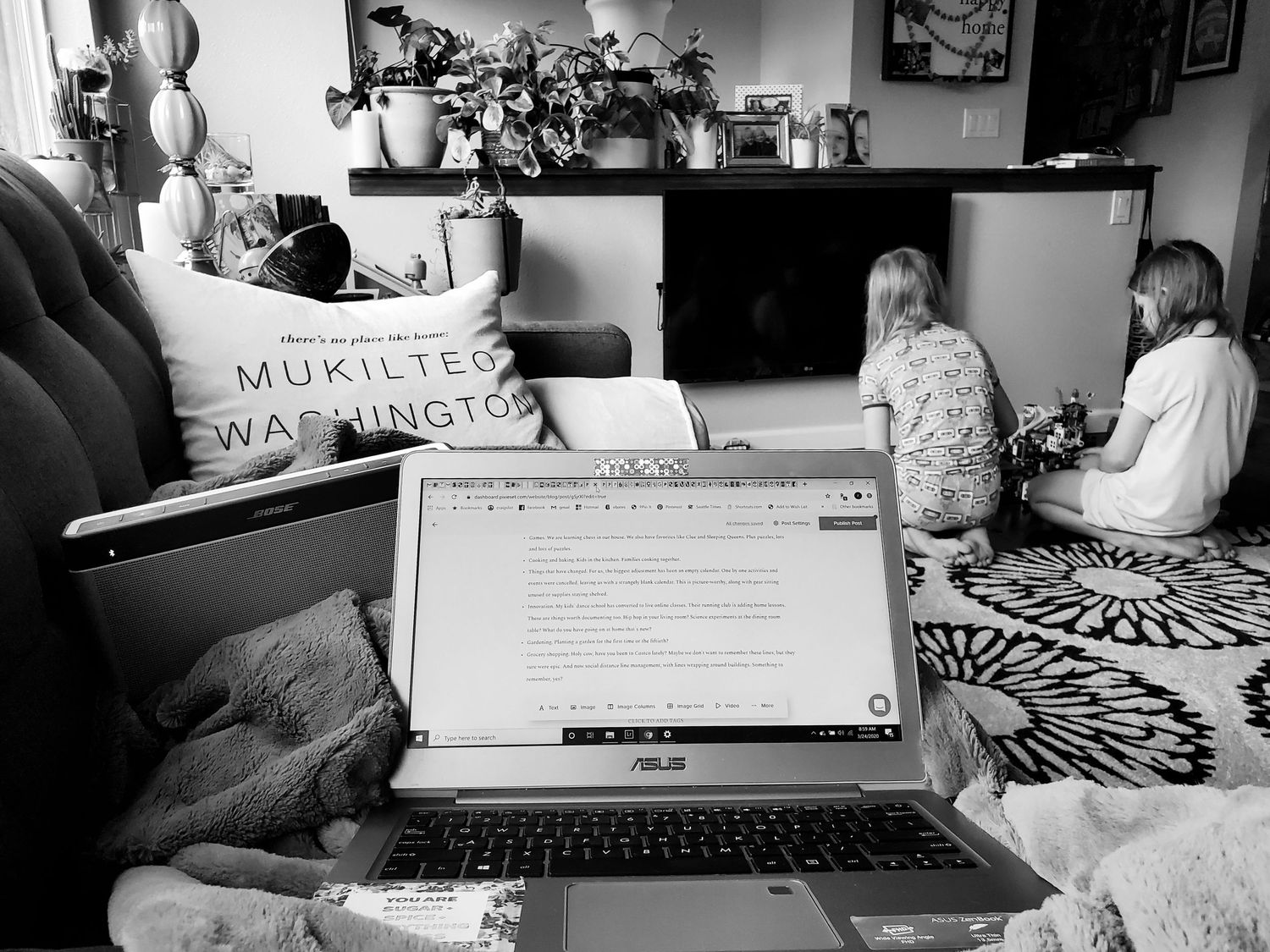 black and white photo of a laptop on a couch and kids playing with Legos in the distance