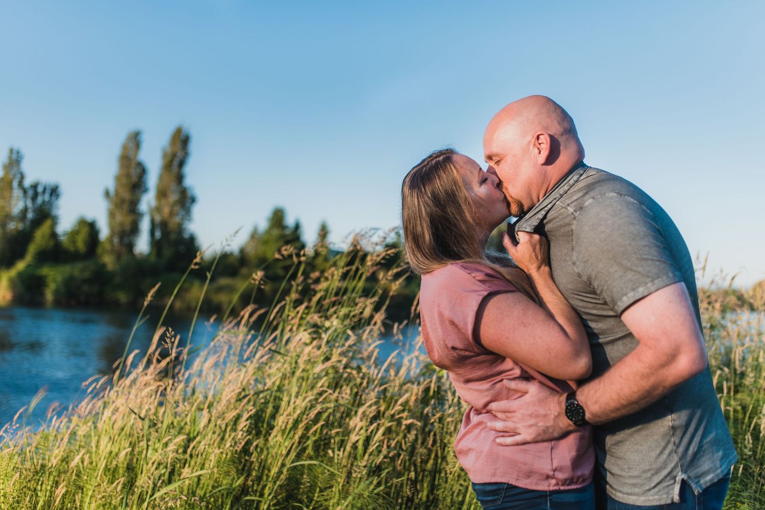 Family photoshoot in tall grass near water during golden hour.