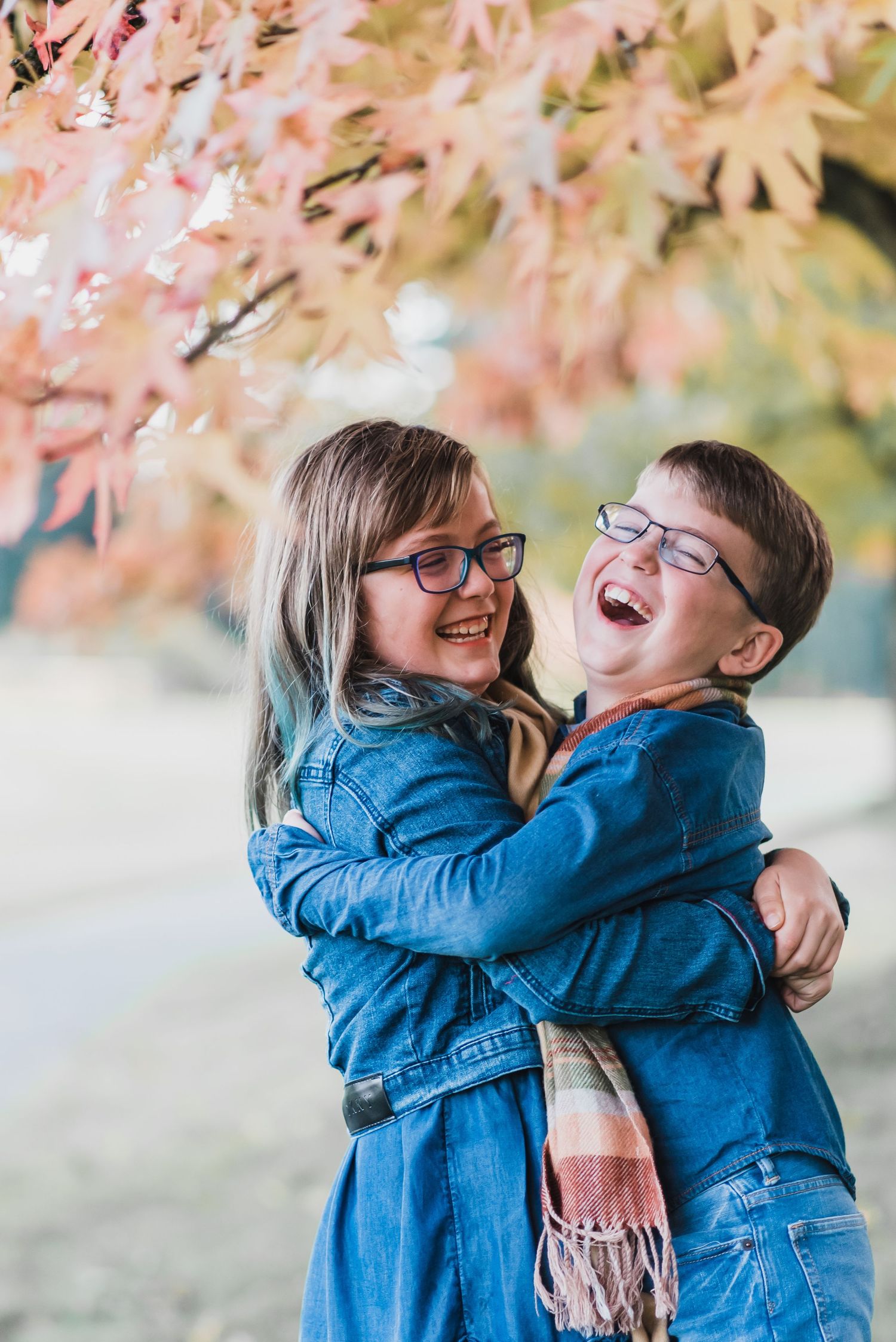 brother and sister laughing and hugging under tree with red leaves