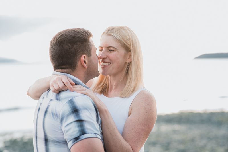 A couple shares romantic moments on a beach at sunset in matching light blue and white outfits.