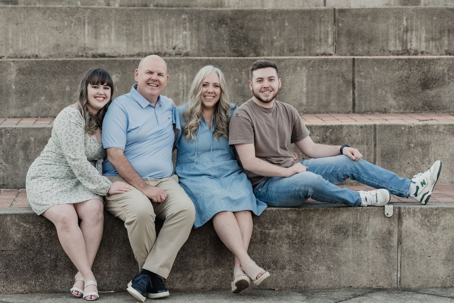 A group wearing coordinating blue and neutral outfits sits casually on concrete steps for an outdoor photo session.