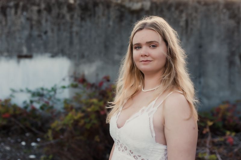 A woman in a white lace dress poses outdoors against a stone wall in a romantic bridal photoshoot.