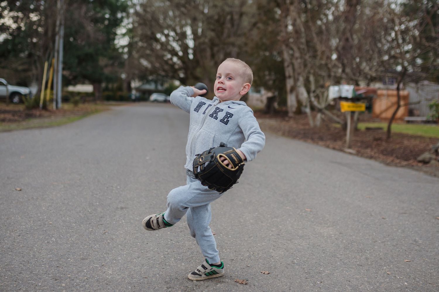 little boy throwing baseball in the middle of the street