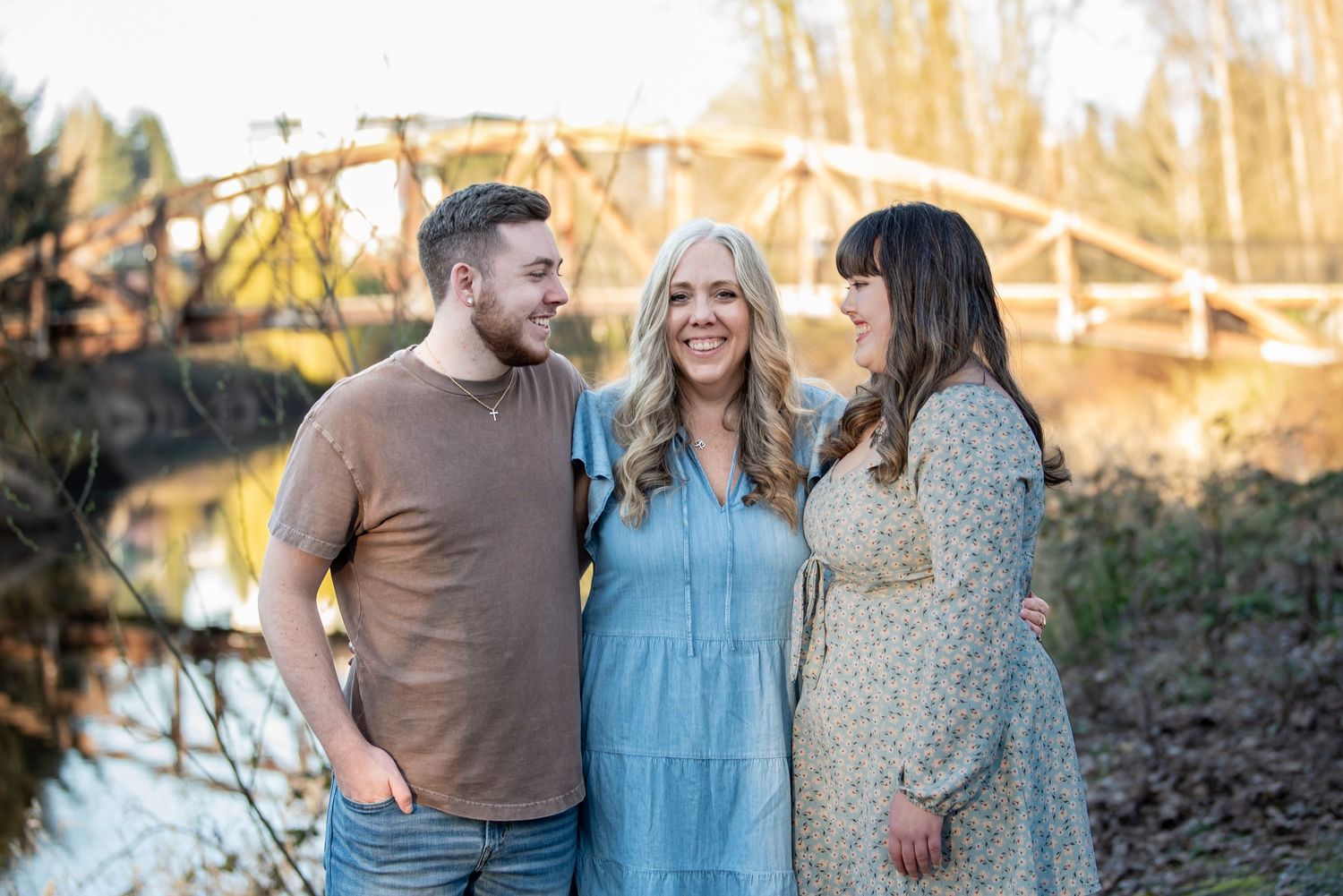 Three friends laughing together outdoors during golden hour photography session in a natural setting.
