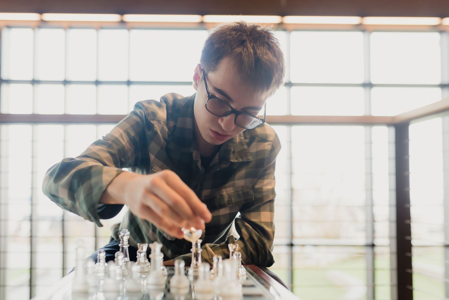 A person in a plaid shirt plays a game of chess, focusing intently on their next strategic move.