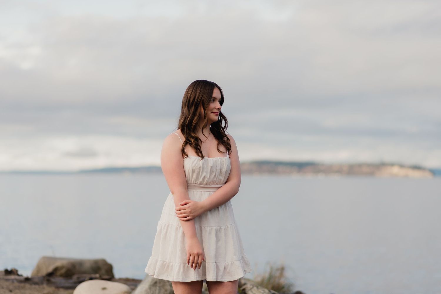 Romantic beach engagement photoshoot showing couple embracing on rocky coastal shore at sunset.