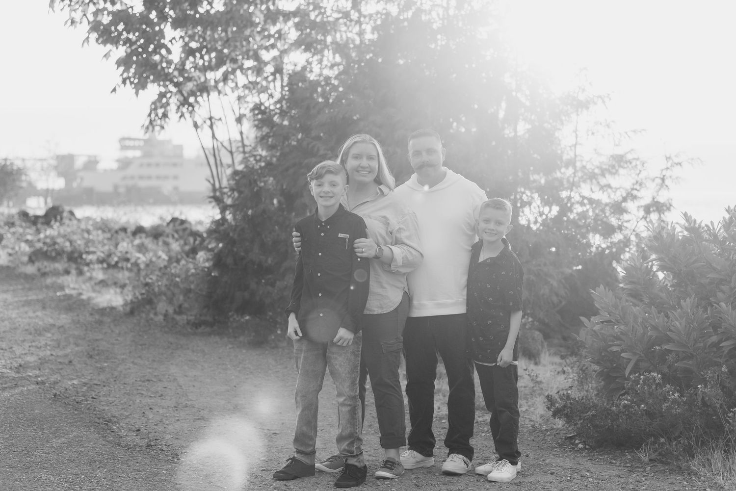 A group of people pose together outdoors in a natural setting with sunlight creating a bright hazy effect.
