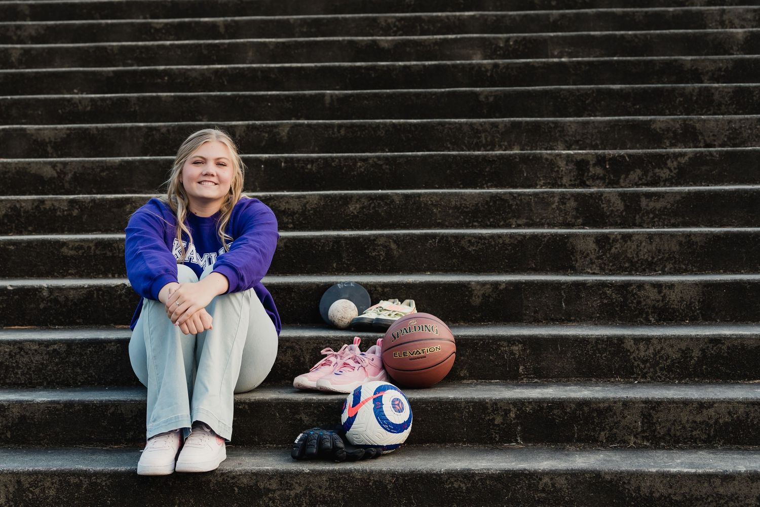 A person sits alone on concrete stadium steps wearing a purple jacket and jeans.