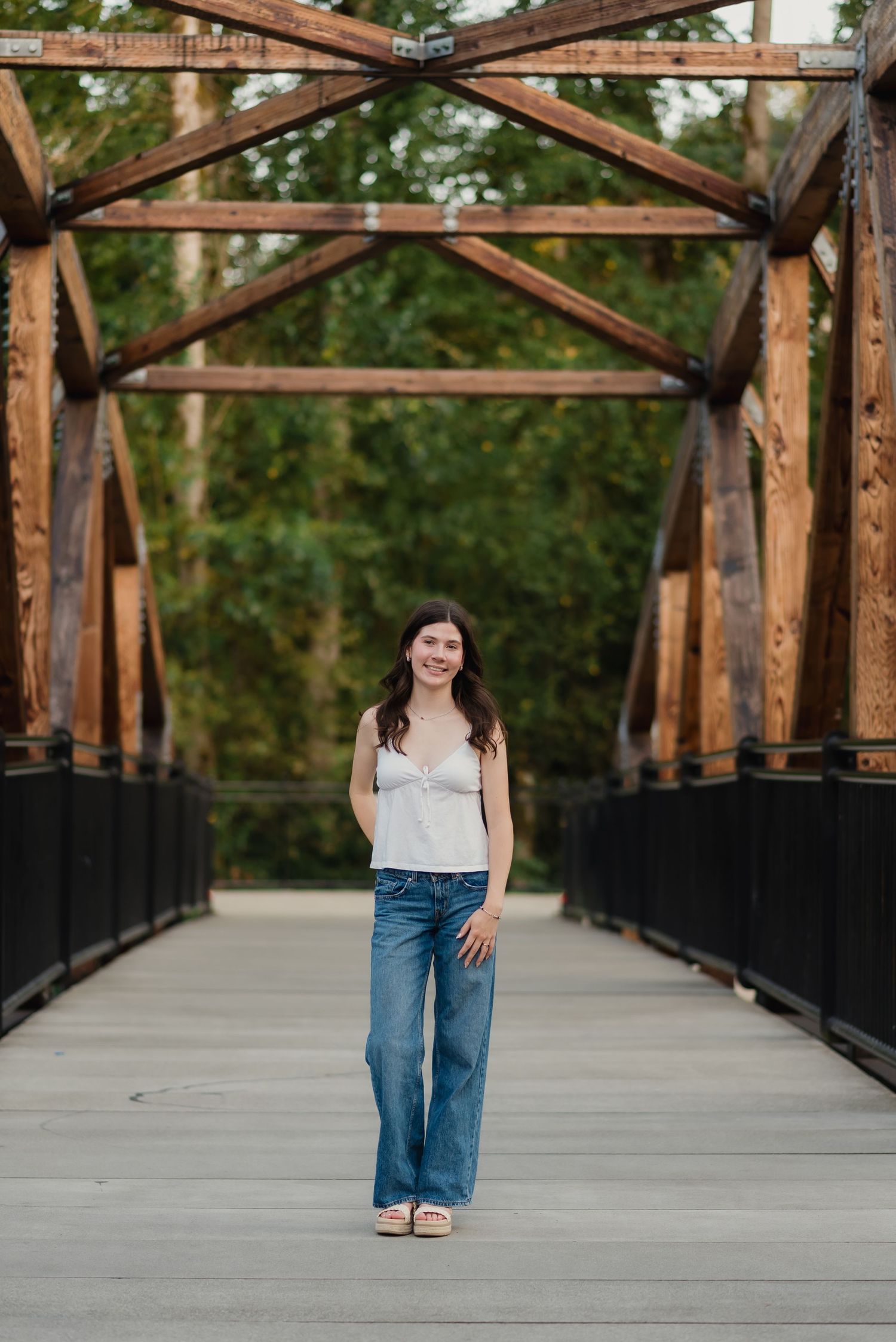 A series of photos showing someone in blue jeans and white top posing on a rustic wooden bridge in a park setting.