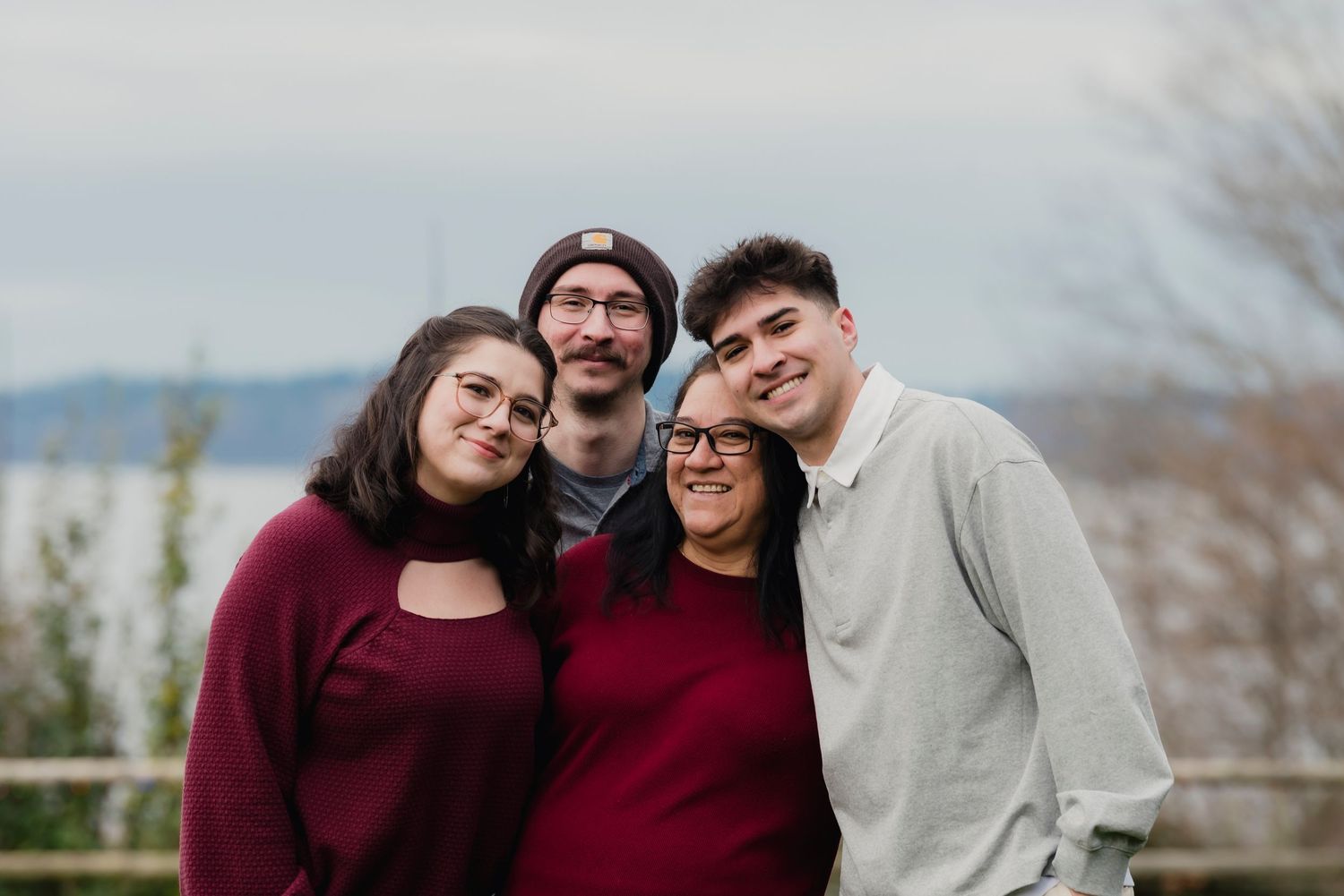 A family wearing burgundy and grey outfits poses together outdoors during a fall photo session.