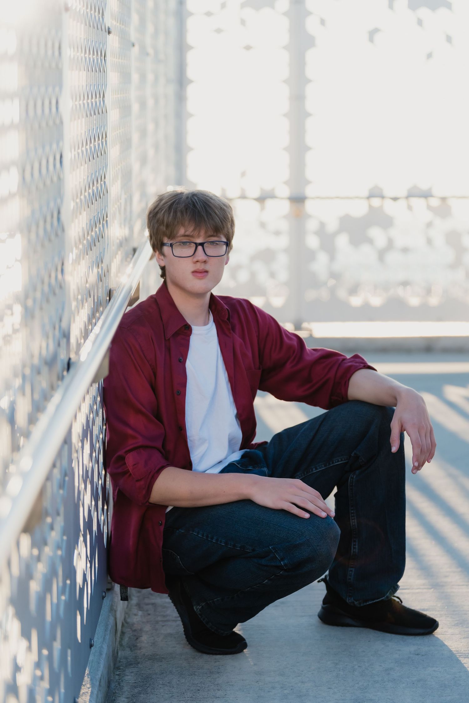 A person in a burgundy jacket and glasses sits casually on a bridge in a series of connected portrait photos.