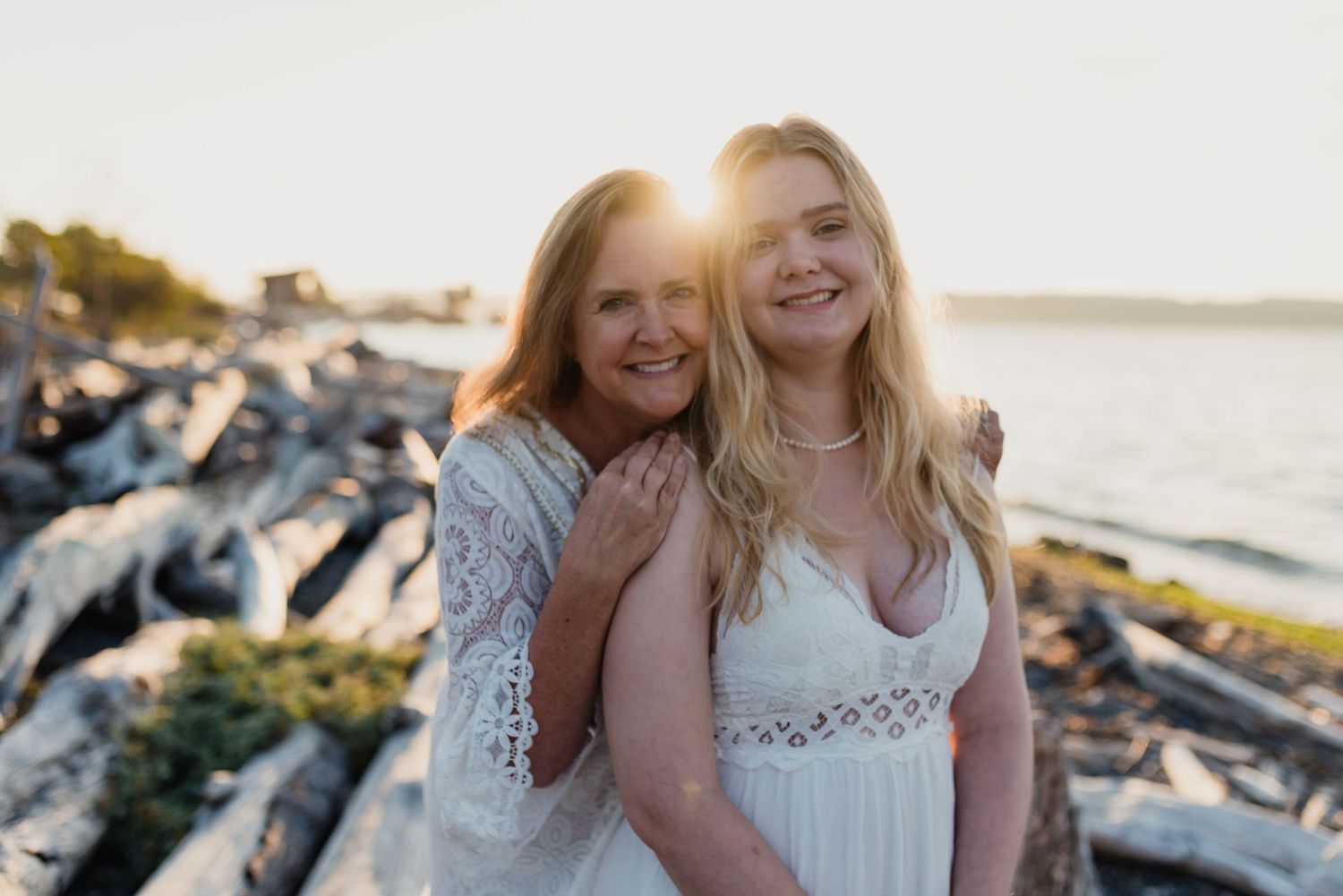 Two people share a joyful moment together while sitting on rocks near the ocean at sunset.