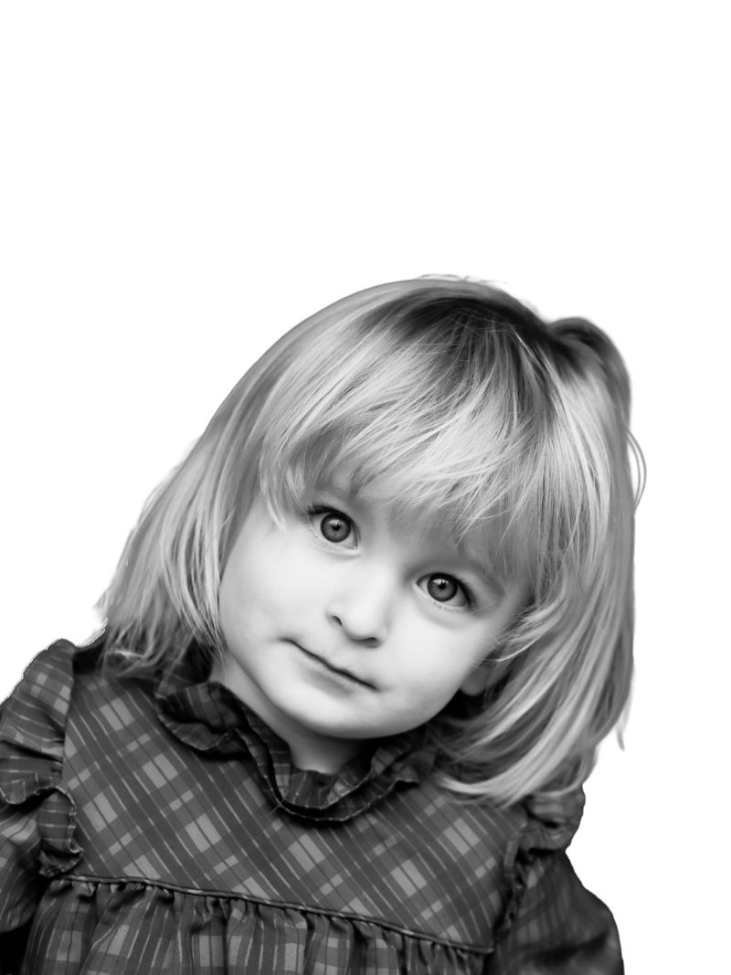 Black and white portrait of a young blonde toddler girl in a plaid dress looking up with a gentle smile.