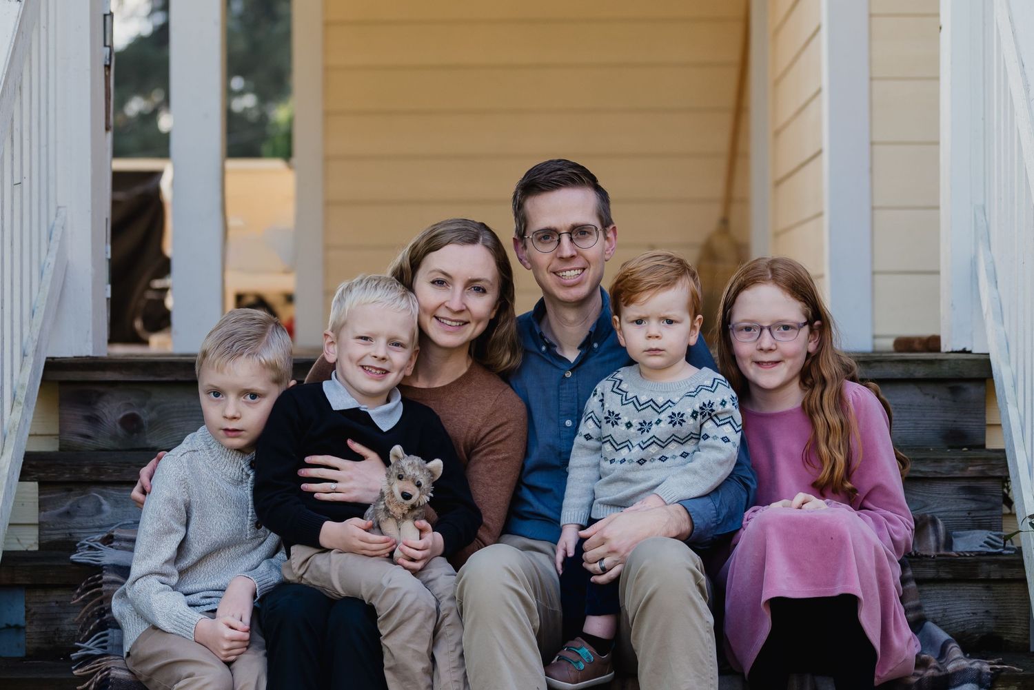 A group of people sit together on a white porch with pillars for a family portrait.